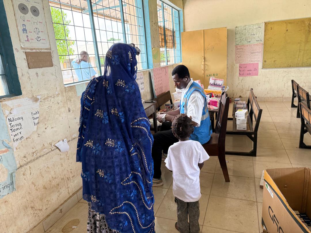 A woman and a young child wait beside a volunteer at the dispensary desk