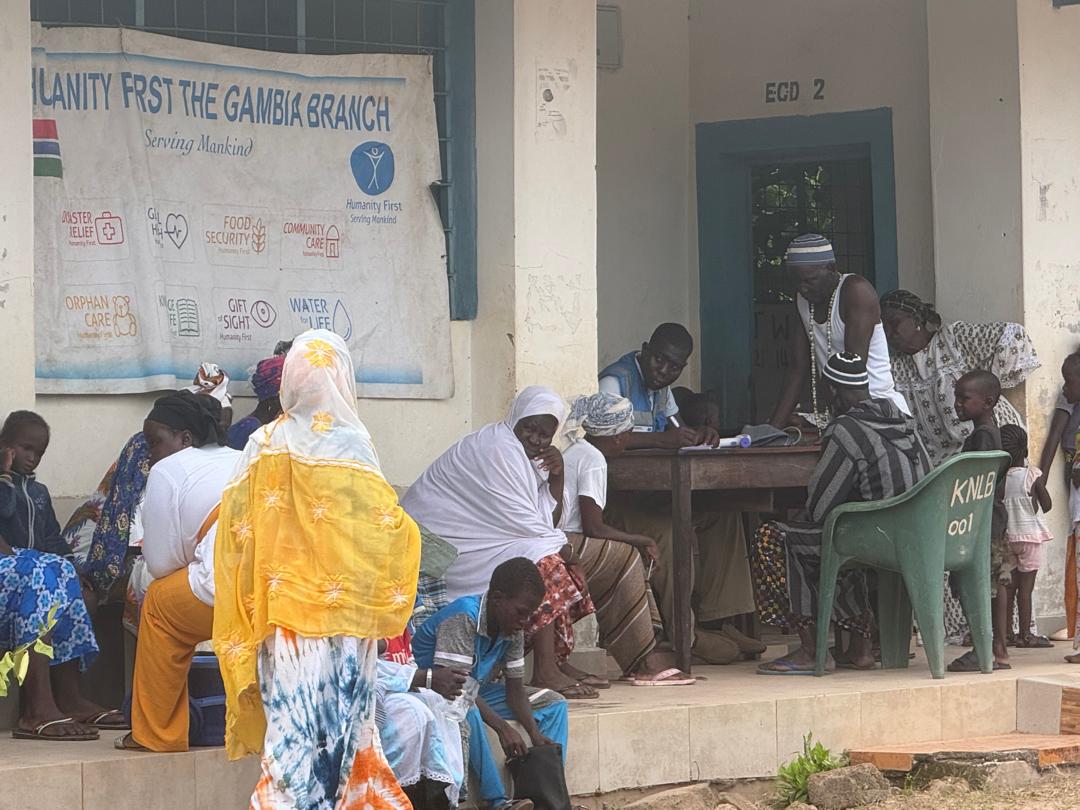 Patients wait on a veranda beneath a Humanity First The Gambia Branch banner