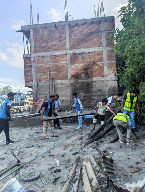 Volunteers carry timber out of a flood-damaged building surrounded by grey silt
