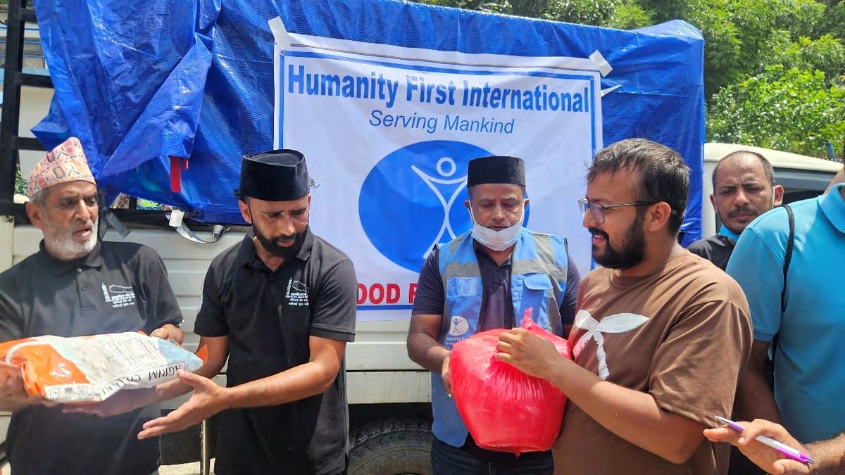 Volunteers hand a food kit to a man at a roadside distribution in Dhading