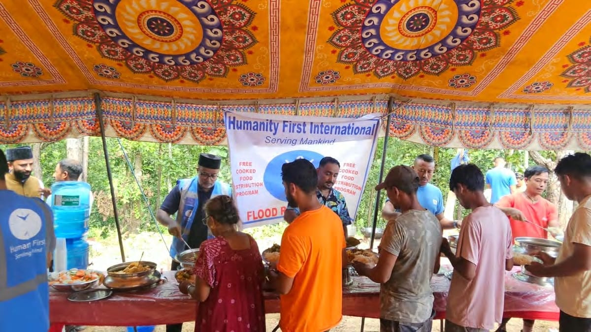 Volunteers serve hot food to a queue of people under a canopy