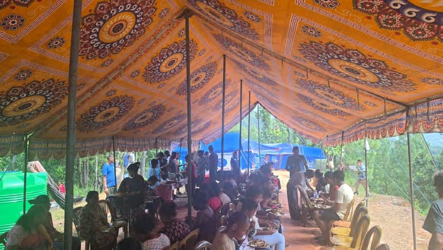 Families eating a hot meal at long tables under the community kitchen canopy