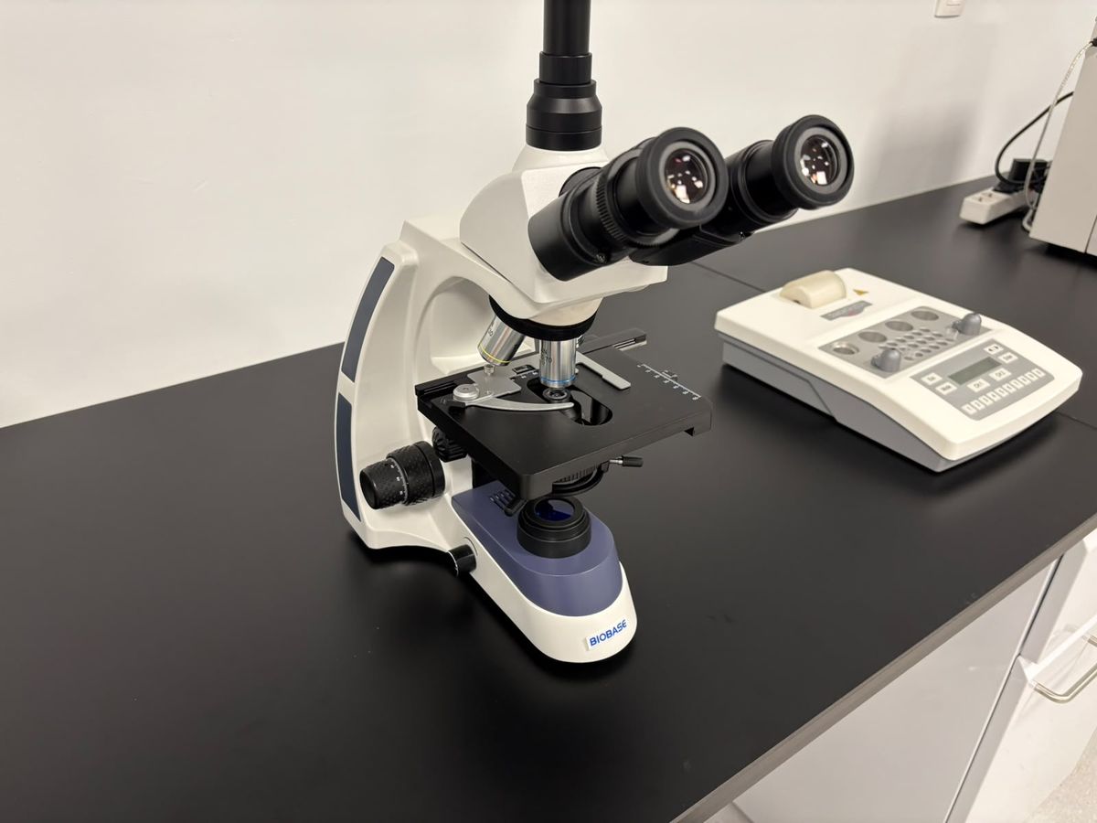 A microscope on the laboratory bench beside a small analyser