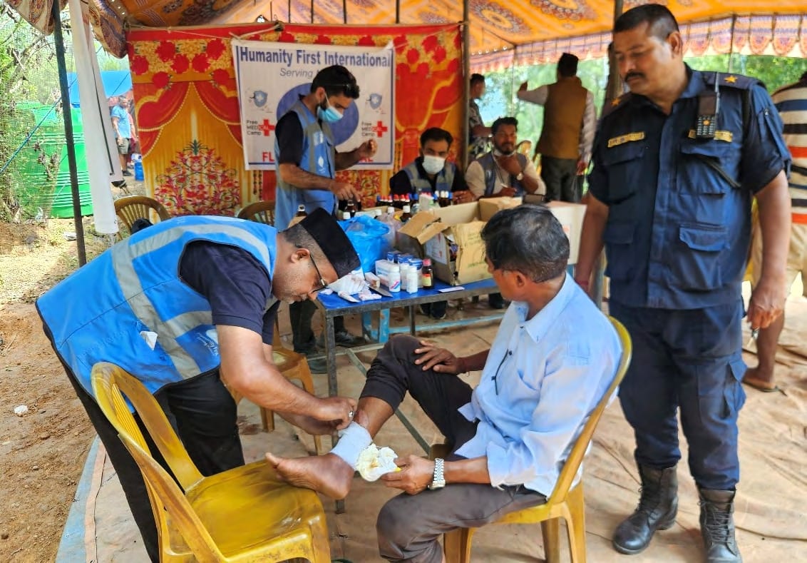 A volunteer dresses a patient's foot at the medical camp while a police officer looks on