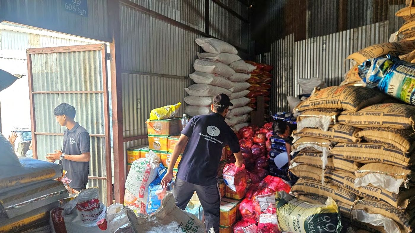 A volunteer carries supplies past stacked sacks of rice in the warehouse where the food kits were packed