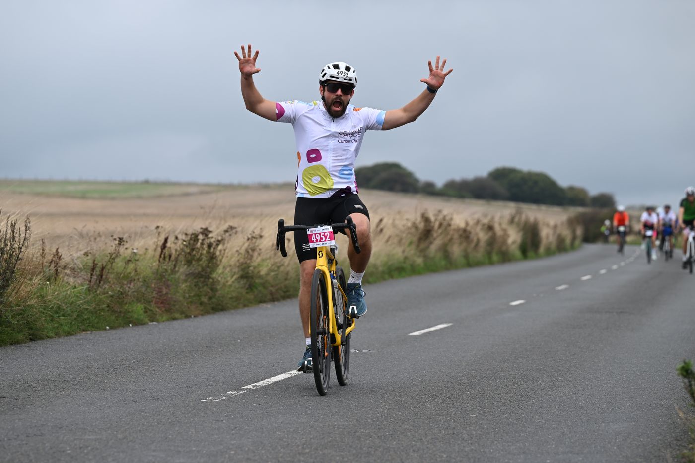 A rider raising both arms on a country road during the London to Brighton Cycle