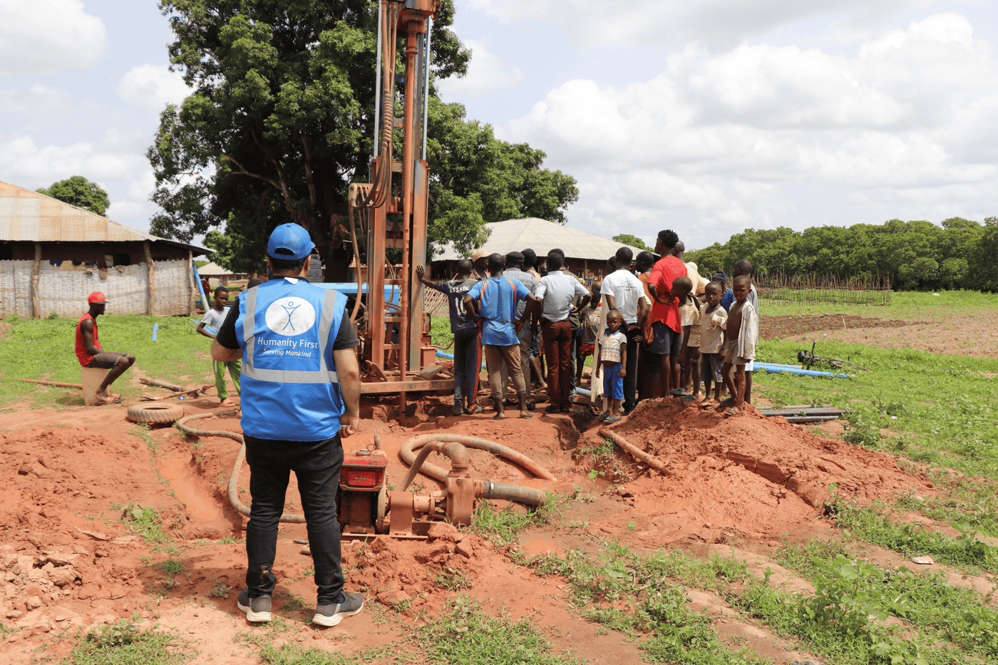 A Humanity First worker oversees a borehole being drilled for a new water well in Guinea-Bissau as the community looks on